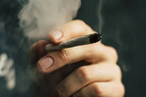 Joint in hand. A man smokes cannabis weed, a . Smoke on a black background. Concepts of medical marijuana use and legalization of the cannabis. — Stock Photo, Image