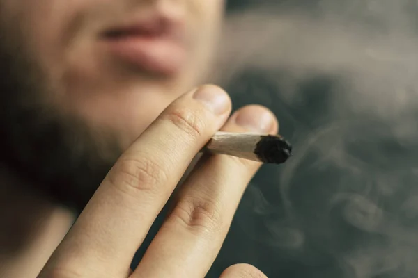 A füst a fekete háttér. Egy férfi dohányzik gyom kannabisz, egy közös és egy könnyebb a kezében. Az orvosi marihuána használata és a kannabisz legalizálása. — Stock Fotó