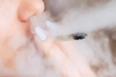 daha hafif ve ortak onun elinde. Bir kadın esrar ot çekiyor bir. Siyah bir arka plan üzerinde duman. Tıbbi esrar kullanım ve yasallaştırma esrar kavramları.