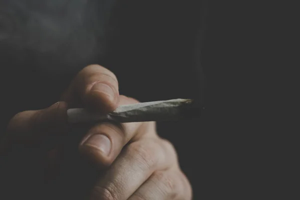 Un homme fume de l'herbe de cannabis, un joint et un briquet dans ses mains. Fumée sur fond noir. Concepts de la consommation de marijuana médicale et légalisation du cannabis . — Photo