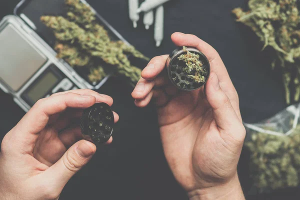 Een man een grinder gebruikt om te slijpen marihuana onkruid tegen een toppen cannabis vintage kleur knoppen cannabis vintage kleur — Stockfoto