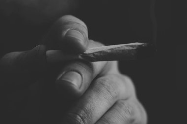 Esrar ot, onun ellerini A adam ortak bir çekiyor. Siyah bir arka plan üzerinde duman. Tıbbi esrar kullanım ve yasallaştırma esrar kavramları. Siyah ve beyaz