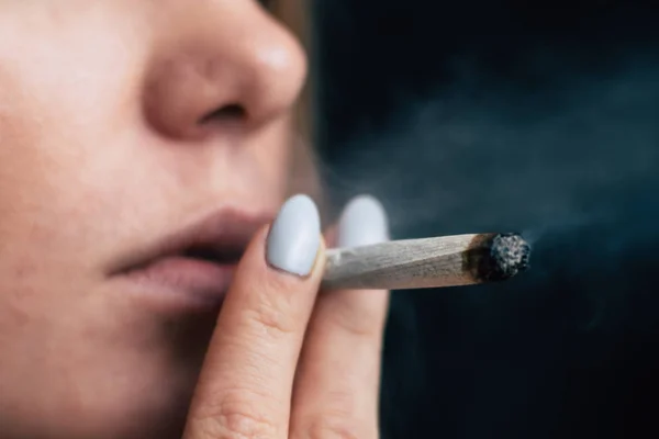 A woman smokes cannabis weed, a joint and a lighter in his hands. Smoke on a black background. Concepts of medical marijuana use and legalization of the cannabis.