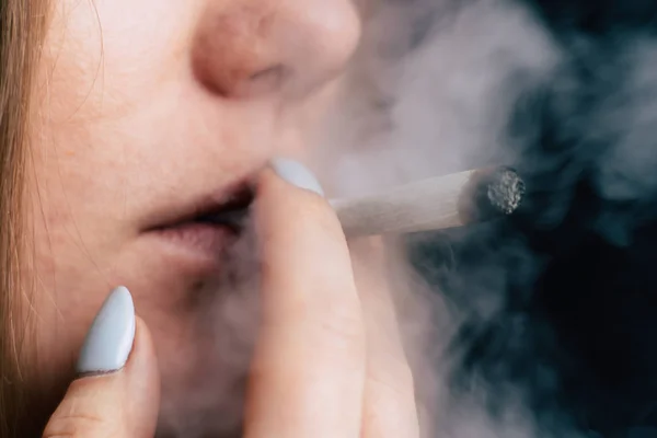 A woman smokes cannabis weed, a joint and a lighter in his hands. Smoke on a black background. Concepts of medical marijuana use and legalization of the cannabis.