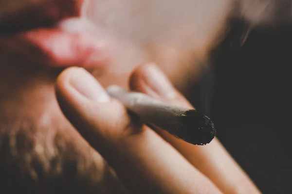 Muž kouří trávu konopí, společnou a zapalovač ve svých rukou. Kouř na černém pozadí. Užívání lékařské marihuany a legalizace konopí. — Stock fotografie