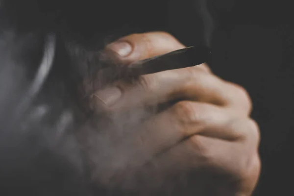 A férfi dohányzik gyom kannabisz egy közös és egy könnyebb a kezében. A füst a fekete háttér. Az orvosi marihuána használata és a kannabisz legalizálása. — Stock Fotó