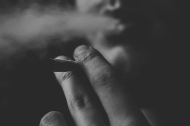 Esrar ot, onun ellerini A adam ortak bir çekiyor. Siyah bir arka plan üzerinde duman. Tıbbi esrar kullanım ve yasallaştırma esrar kavramları. Siyah ve beyaz