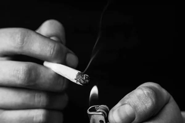 Gezamenlijke in man hand. Een man rookt cannabis onkruid, een. Roken op een zwarte achtergrond. Begrippen medisch marihuanagebruik en legalisatie van de cannabis. Zwart-wit — Stockfoto