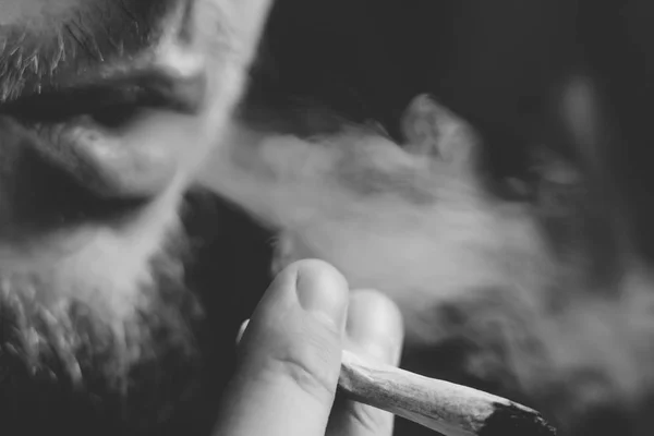 Erva de cannabis, um charro nas mãos Um homem fuma. Fumar em um fundo preto. Conceitos de uso medicinal de maconha e legalização do canabis.Preto e branco — Fotografia de Stock