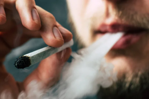 A férfi dohányzik gyom kannabisz egy közös és egy könnyebb a kezében. A füst a fekete háttér. Az orvosi marihuána használata és a kannabisz legalizálása. — Stock Fotó