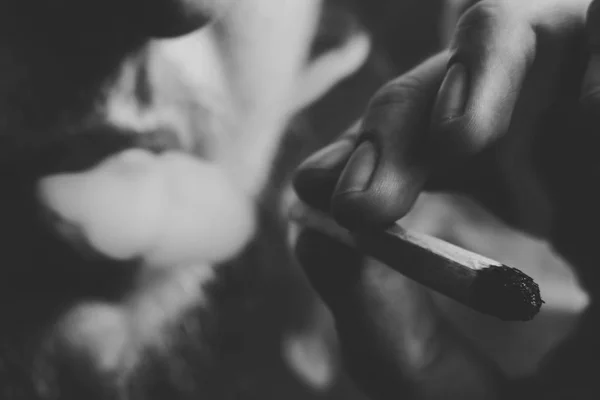 Ένας άνθρωπος καπνίζει κάνναβη ζιζανίων, ένα κοινό και ένα ελαφρύτερο στα χέρια του. Καπνού σε μαύρο φόντο. Έννοιες της ιατρική χρήση μαριχουάνα και τη νομιμοποίηση της κάνναβης. Μαύρο και άσπρο — Φωτογραφία Αρχείου