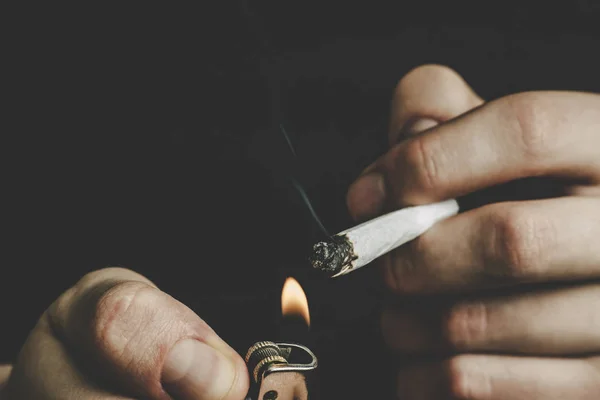 Cannabis onkruid, een joint in zijn handen A man rookt. Roken op een zwarte achtergrond. Concepten van medisch marihuanagebruik en legalisatie van de cannabis. — Stockfoto