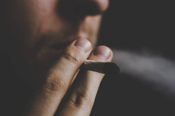 smokes weed cannabis, A man joint in his hands. Smoke on a black background. Concepts of medical marijuana use and legalization of the cannabis.