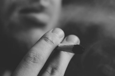 Esrar ot, onun ellerini A adam ortak bir çekiyor. Siyah bir arka plan üzerinde duman. Tıbbi esrar kullanım ve yasallaştırma esrar kavramları. Siyah ve beyaz