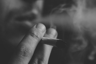 esrar otu A adam sigara, bir ortak ve bir çakmak onun elinde. Siyah bir arka plan üzerinde duman. Tıbbi esrar kullanım ve yasallaştırma esrar kavramları. Siyah ve beyaz