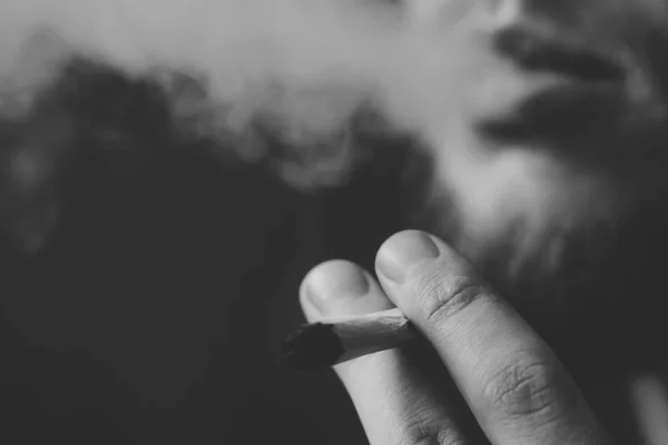 Fume de l'herbe de cannabis, un joint et un briquet dans ses mains. Fumée sur fond noir. Concepts de la consommation de marijuana médicale et de la légalisation du cannabis.Noir et blanc — Photo