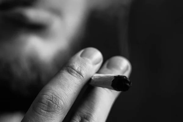 Herbe de cannabis, un joint dans ses mains Un homme fume. Fumée sur fond noir. Concepts de la consommation de marijuana médicale et de la légalisation du cannabis.Noir et blanc — Photo