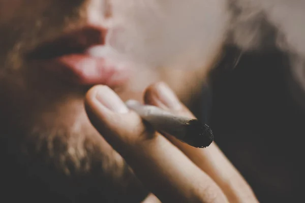 Kouř na černém pozadí. Muž kouří konopí plevel, společné a zapalovač ve svých rukou. Užívání lékařské marihuany a legalizace konopí. — Stock fotografie