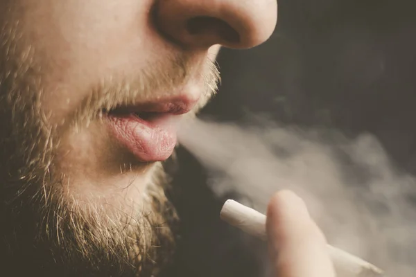 A man smokes cannabis weed, a joint and a lighter in his hands. Smoke on a black background. Concepts of medical marijuana use and legalization of the cannabis. — Stock Photo, Image