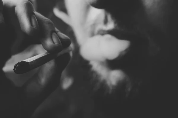 Herbe de cannabis, un joint dans ses mains Un homme fume. Fumée sur fond noir. Concepts de la consommation de marijuana médicale et de la légalisation du cannabis.Noir et blanc — Photo