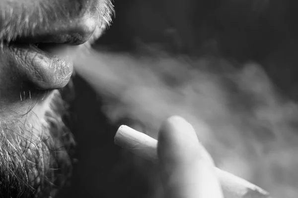 Курит марихуану, мужской косяк в руках. Дым на черном фоне. Концепции использования медицинской марихуаны и легализации конопли. — стоковое фото