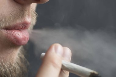 Esrar ot, onun ellerini A adam ortak bir çekiyor. Siyah bir arka plan üzerinde duman. Tıbbi esrar kullanım ve yasallaştırma esrar kavramları.