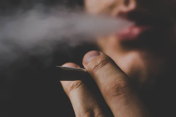 Um homem fuma maconha um charro e um isqueiro nas mãos. Fumar em um fundo preto. Conceitos de uso medicinal de maconha e legalização da cannabis . — Fotografia de Stock