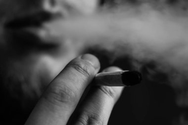 Bir adam sigara esrar esrar, esrar ve çakmak elinde. Siyah bir arka plan üzerinde duman. Tıbbi esrar kullanım ve yasallaştırma esrar kavramları. Siyah ve beyaz