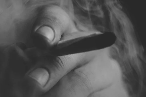 En man röker cannabis ogräs, en gemensam och en tändare i handen. Rök på en svart bakgrund. Begreppet medicinsk marijuana användning och legalisering av cannabis. Svart och vitt — Stockfoto