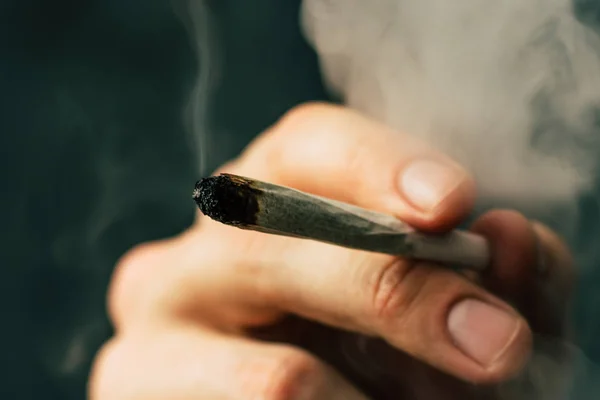 Közös az ember kezében. A férfi dohányzik kannabisz füvet, egy. A füst a fekete háttér. Az orvosi marihuána használata és a kannabisz legalizálása. — Stock Fotó