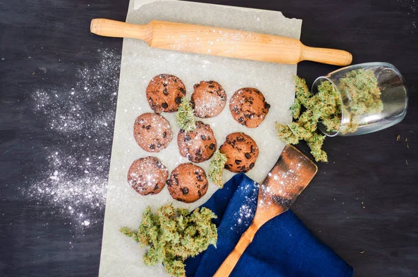 Cookies med cannabis och knoppar av marijuana på bordet. Begreppet matlagning med cannabisblad. Behandling av medicinsk marijuana för användning i livsmedel ovanifrån, på en svart bakgrund — Stockfoto