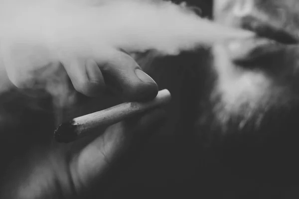 Fumée sur fond noir. Un homme fume de l'herbe de cannabis, un joint et un briquet dans ses mains. Concepts de la consommation de marijuana médicale et de la légalisation du cannabis.Noir et blanc — Photo