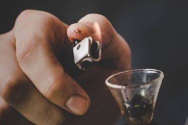 nargile ve onun elinde bir çakmak. Bir adam esrar ot, duman siyah bir zemin üzerine çekiyor. Tıbbi esrar kullanım ve yasallaştırma esrar kavramları.