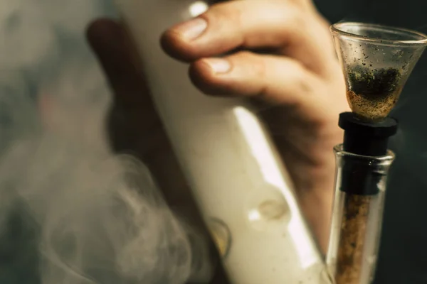 Fogalmak és a kannabisz legalizálása orvosi marihuána. Egy férfi dohányzik gyom kannabisz, egy bong, és egy könnyebb a kezében. Füst a fekete háttér. — Stock Fotó
