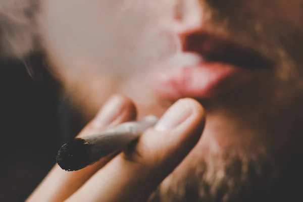 Muž kouří konopí plevel, společné a zapalovač ve svých rukou. Kouř na černém pozadí. Užívání lékařské marihuany a legalizace konopí. — Stock fotografie