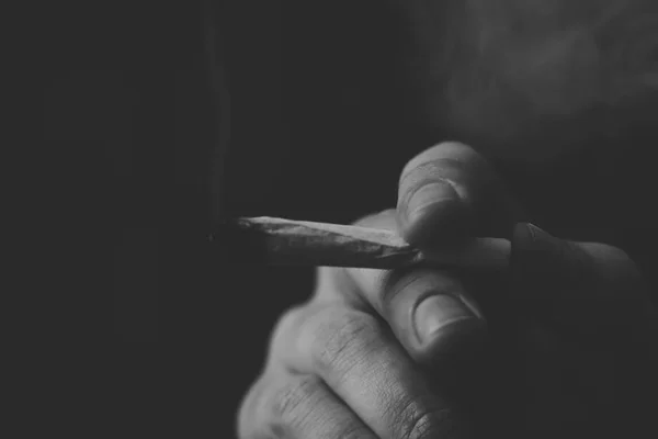 Un hombre fuma marihuana, un porro y un encendedor en sus manos. Humo sobre fondo negro. Conceptos de uso medicinal de la marihuana y legalización del cannabis.Blanco y negro —  Fotos de Stock