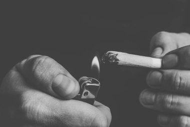 Bir adam sigara esrar esrar, esrar ve çakmak elinde. Siyah bir arka plan üzerinde duman. Tıbbi esrar kullanım ve yasallaştırma esrar kavramları. Siyah ve beyaz
