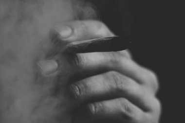 elinde ortak. Bir adam esrar ot çekiyor bir. Siyah bir arka plan üzerinde duman. Tıbbi esrar kullanım ve yasallaştırma esrar kavramları. Siyah ve beyaz