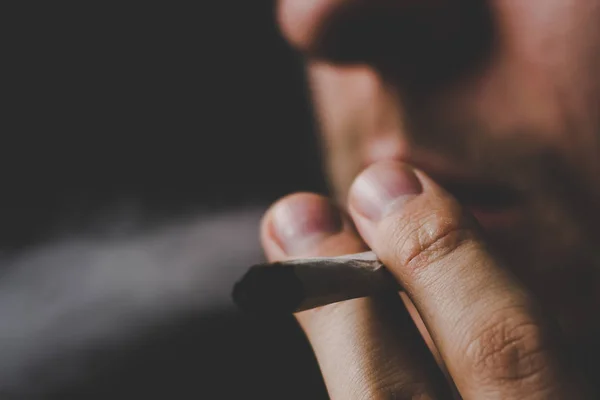Ein Mann raucht Cannabiskraut, einen Joint und ein Feuerzeug in den Händen. Rauch auf schwarzem Hintergrund. Konzepte des medizinischen Marihuana-Konsums und der Legalisierung von Cannabis. — Stockfoto