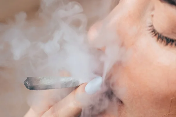 Kannabisz A gyom nő dohányzik, egy közös és egy könnyebb a kezében. A füst a fekete háttér. Az orvosi marihuána használata és a kannabisz legalizálása. — Stock Fotó