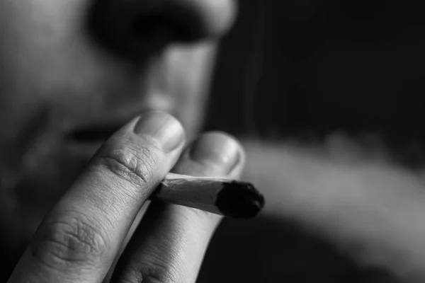 Conceitos de uso medicinal de maconha e legalização da cannabis. Fumar em um fundo preto. Um homem fuma maconha, um charro e um isqueiro em suas mãos.Preto e branco — Fotografia de Stock