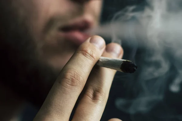 Concepts of medical marijuana use and legalization of the cannabis. Smoke on a black background. A man smokes cannabis weed, a joint and a lighter in his hands. — Stock Photo, Image