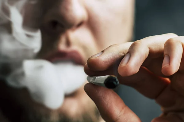 Egy férfi dohányzik gyom kannabisz, egy közös és egy könnyebb a kezében. A füst a fekete háttér. Az orvosi marihuána használata és a kannabisz legalizálása. — Stock Fotó