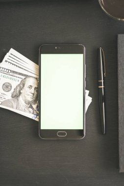 Smartphone ile chromakey anahtarlama ve bir siyah mockup için yüz dolar banknotlar ABD ile ahşap masa dokulu. Yeni Finans teknolojileri ve iş haberleri kavramları. Dikey .