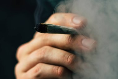 Bir adam sigara esrar esrar, esrar ve çakmak elinde. Siyah bir arka plan üzerinde duman. Tıbbi esrar kullanım ve yasallaştırma esrar kavramları.