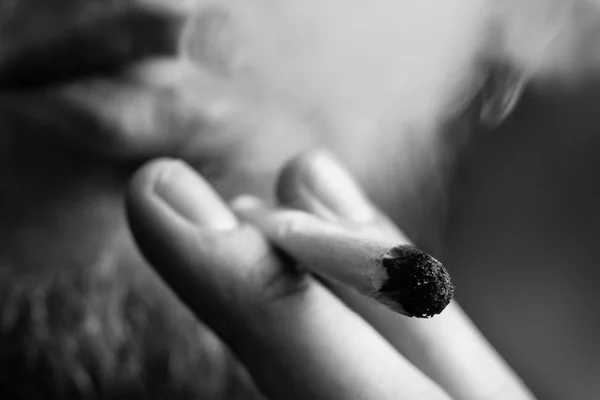 Cannabis onkruid, een joint in zijn handen A man rookt. Roken op een zwarte achtergrond. Begrippen medisch marihuanagebruik en legalisatie van de cannabis. Zwart-wit — Stockfoto