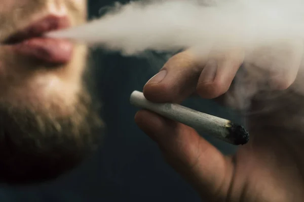 Concepts of medical marijuana use and legalization of the cannabis. Smoke on a black background. A man smokes cannabis weed, a joint and a lighter in his hands. — Stock Photo, Image