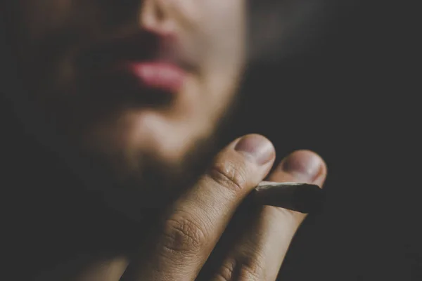 A man smokes cannabis weed, a joint and a lighter in his hands. Smoke on a black background. Concepts of medical marijuana use and legalization of the cannabis. — Stock Photo, Image