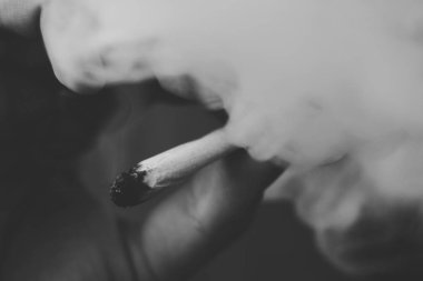 Bir adam ot Esrar sigara esrar ve çakmak onun ellerinde. Siyah bir arka plan üzerinde duman. Tıbbi esrar kullanım ve yasallaştırma esrar kavramları. Siyah ve beyaz