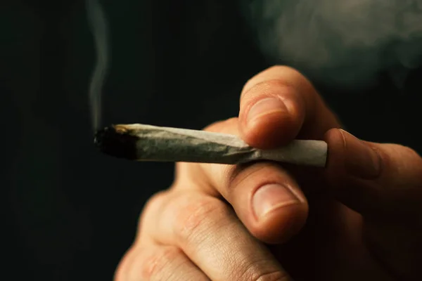 Έννοιες της ιατρική χρήση μαριχουάνα και τη νομιμοποίηση της κάνναβης. Καπνού σε μαύρο φόντο. Ένας άνθρωπος καπνίζει κάνναβη ζιζανίων, ένα κοινό και ένα ελαφρύτερο στα χέρια του. — Φωτογραφία Αρχείου